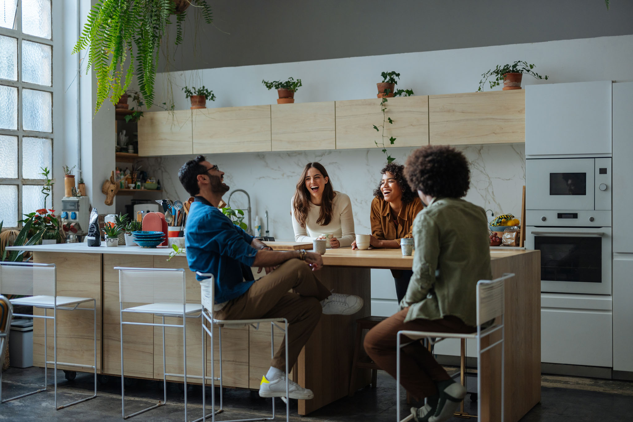 Cheerful friends laughing and talking, sitting in modern kitchen